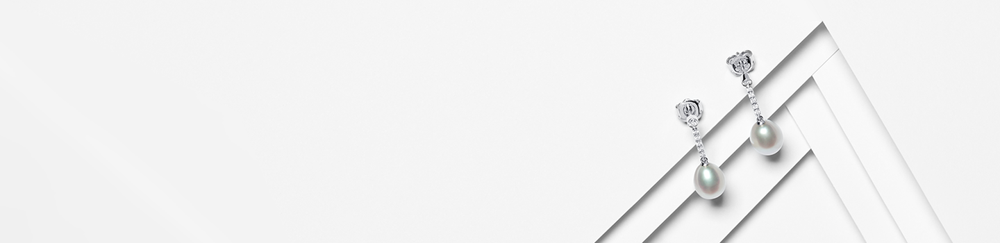 A pair of Birks pearl and diamond earrings on a white layered background.